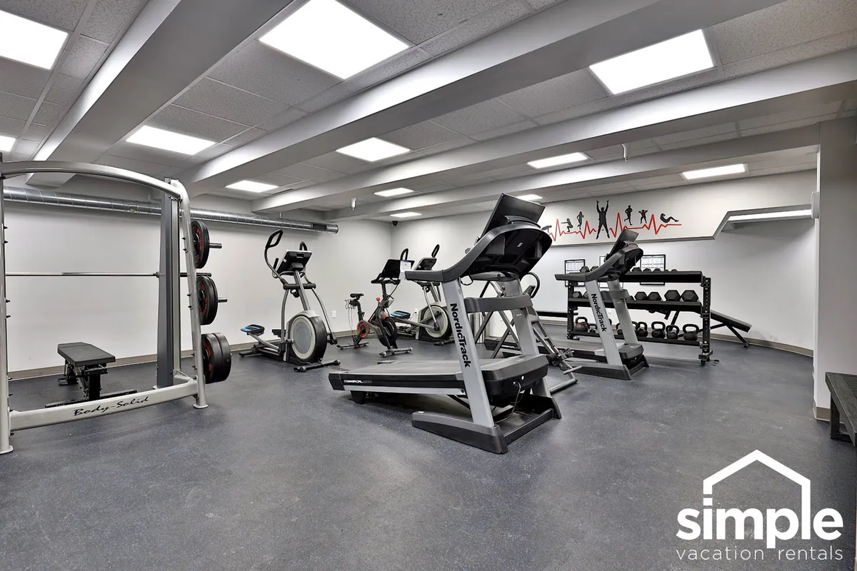 A well-equipped fitness center featuring weightlifting machines, elliptical equipment, exercise mats, and motivational wall art. The open, energetic space supports both solo workouts and small group sessions.