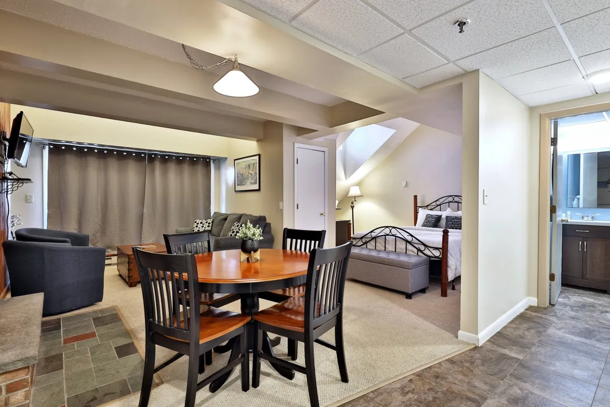 This image showcases an inviting interior that seamlessly combines the dining, seating, and sleeping areas. The queen bed, dining table, and cozy seating area are all visible, highlighting the multifunctional nature of the studio. Natural light filters in, creating a welcoming and serene atmosphere, while the smart TV is present for entertainment.