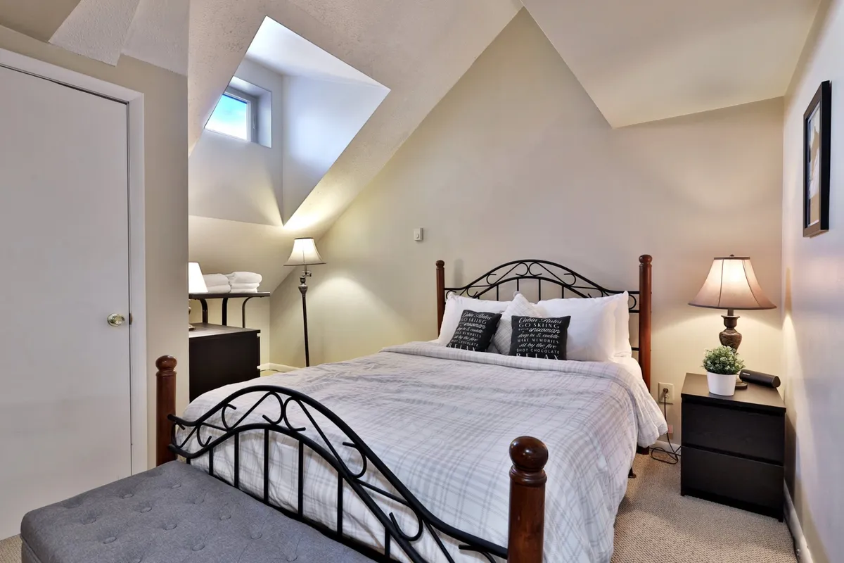 This scene focuses on the sleeping area with a comfortable bed, ambient lighting from bedside lamps, and a window letting in natural light. Decorative accents and a nightstand contribute to a restful, home-like vibe.