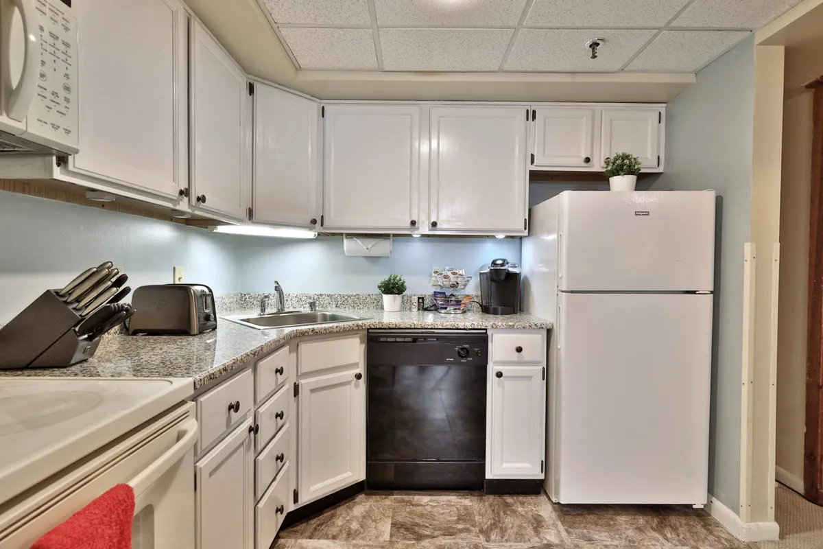 This image highlights a welcoming kitchen with granite countertops, white cabinetry, and a black dishwasher. Kitchen appliances are visible, and the space is arranged for easy meal preparation and social interaction.