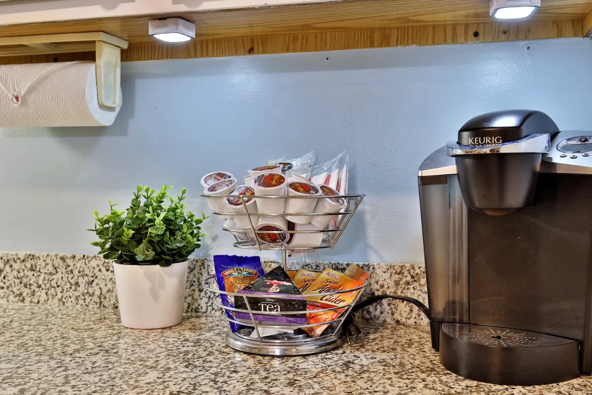 A close-up shot of a Keurig coffee maker and K-cup holder, accented by a potted plant, sits on a kitchen counter. It evokes the freshness of morning coffee and the casual comfort of the space.