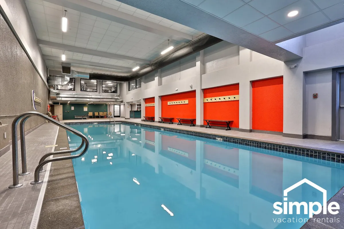 This image depicts a vibrant indoor swimming pool area, featuring bright red walls, a spacious pool, and a comfortable seating area along the side. The inviting setting signals opportunities for family fun and relaxation, with space for both active play and lounging.