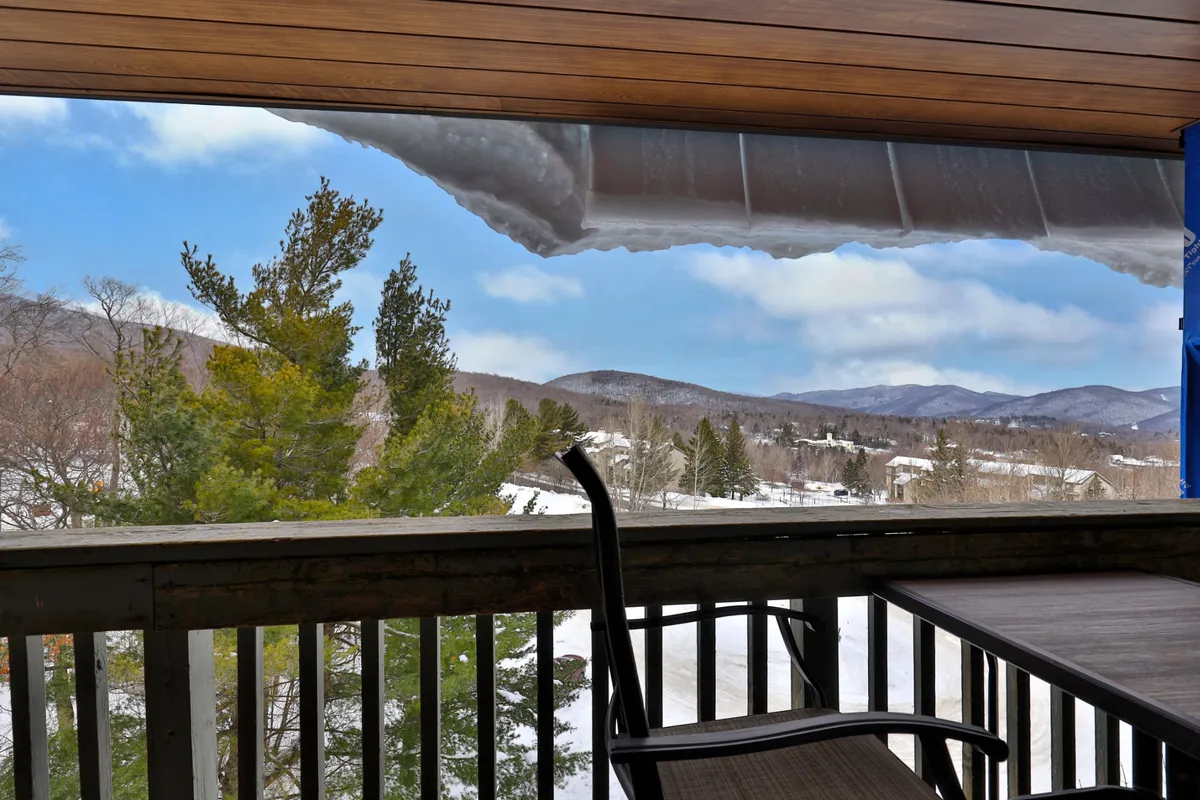 A calm and peaceful vista from a balcony overlooking a pristine, snow-blanketed landscape with distant mountain peaks. The wooden railing suggests a cozy place to pause and enjoy the view, hinting at relaxation after outdoor adventures.