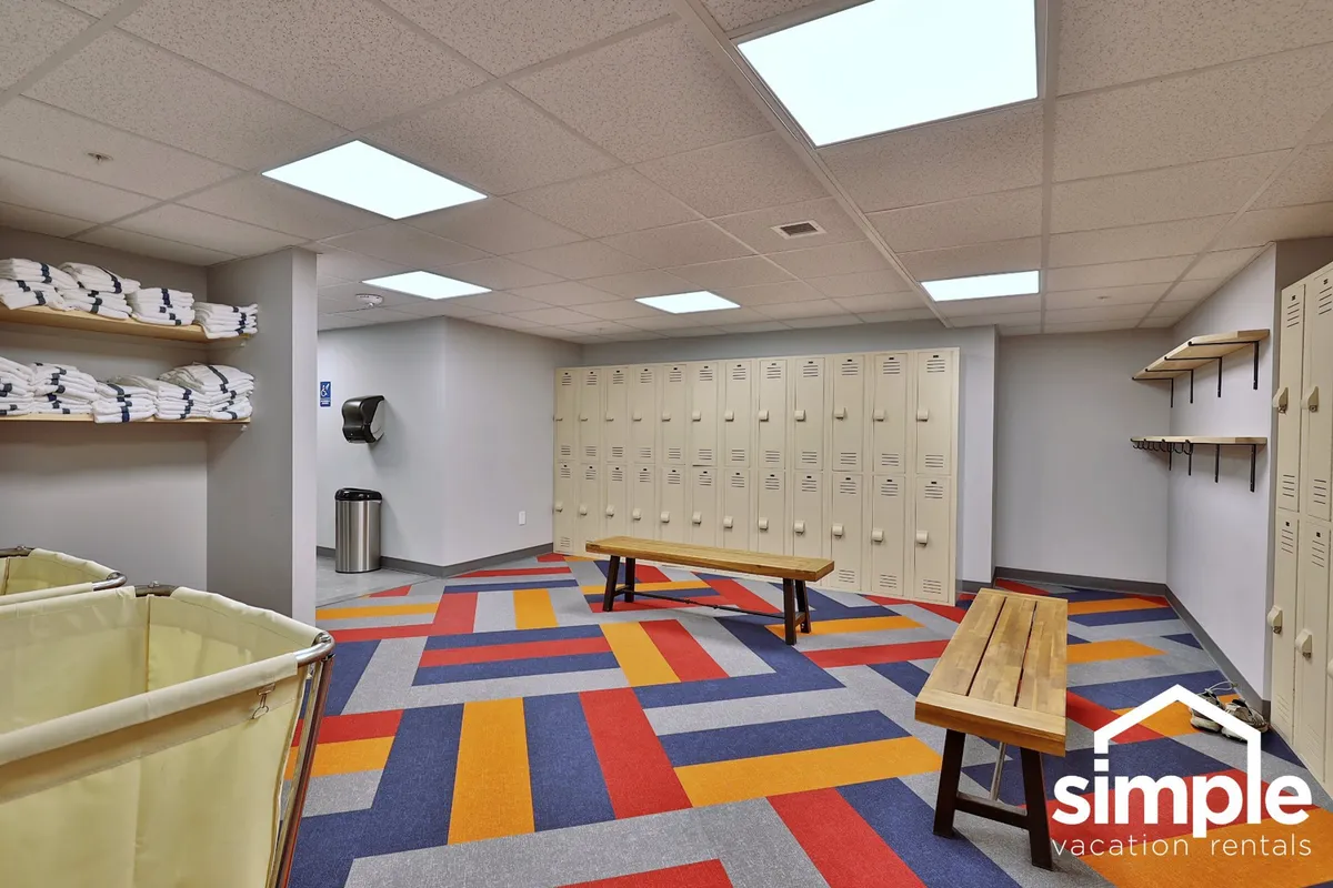 A cheerful, practical locker and changing area with colorful patterned flooring, wooden benches, and neatly stacked towels. The space is organized and clean, making it ideal for prepping before or after pool time or outdoor excursions.