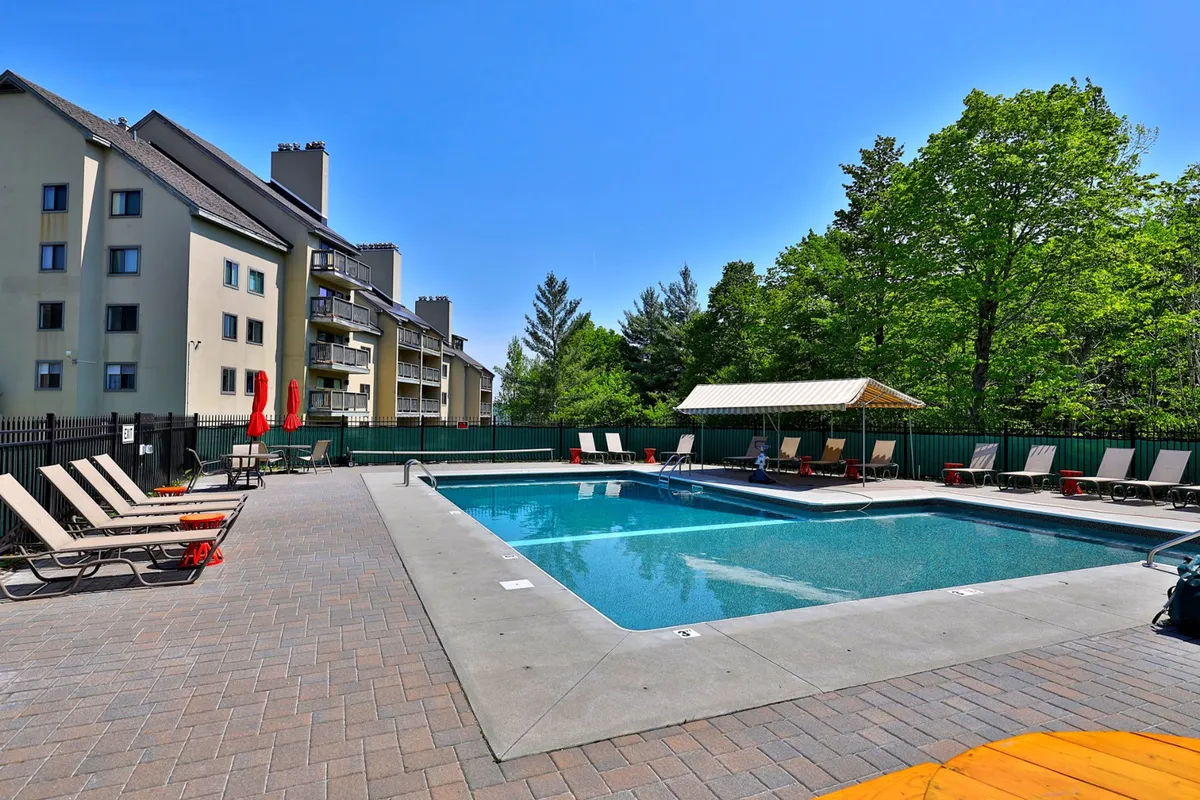 An outdoor swimming pool surrounded by lush greenery, lounge chairs, and a charming poolside gazebo. The inviting setup hints at sunny days, social gatherings, and moments of relaxation under the open sky.