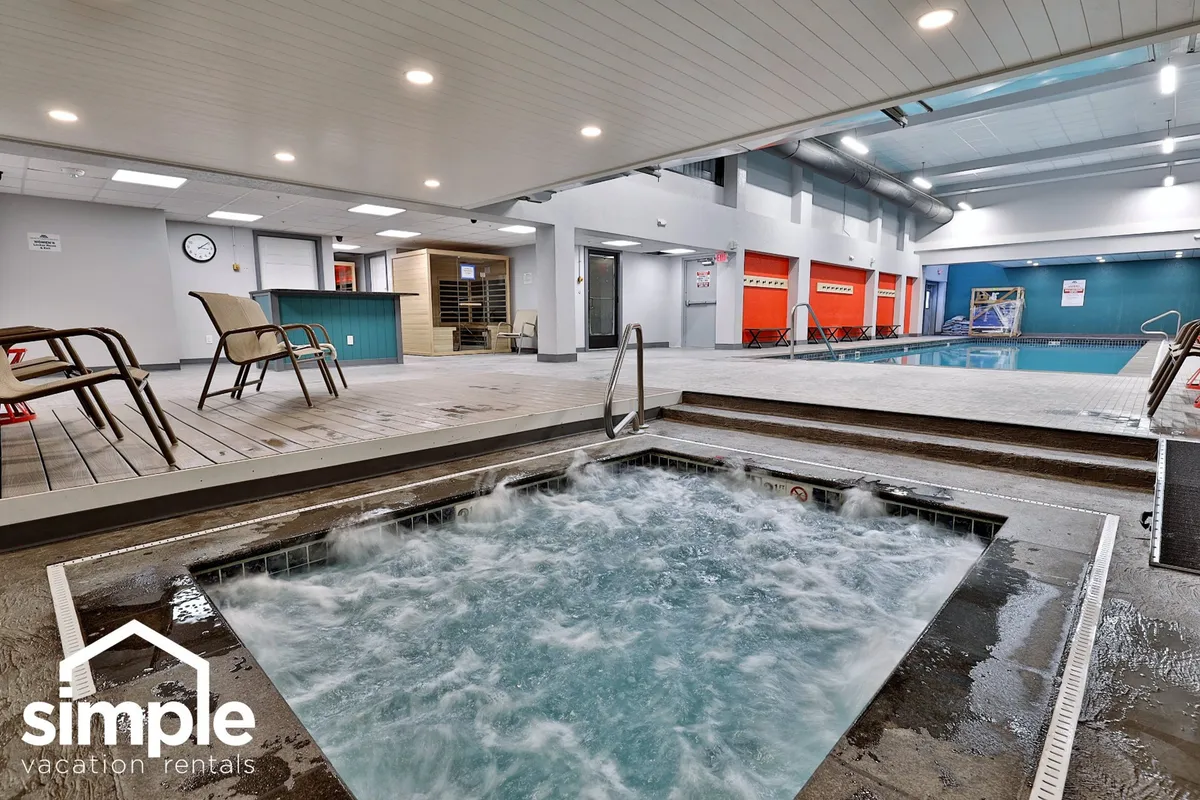 This image features an inviting indoor swimming pool with a relaxing hot tub adjacent to it. Lounge chairs are positioned nearby, creating a tranquil environment ideal for both relaxation and socializing. The space is well-lit and designed to encourage guests to unwind after an active day.